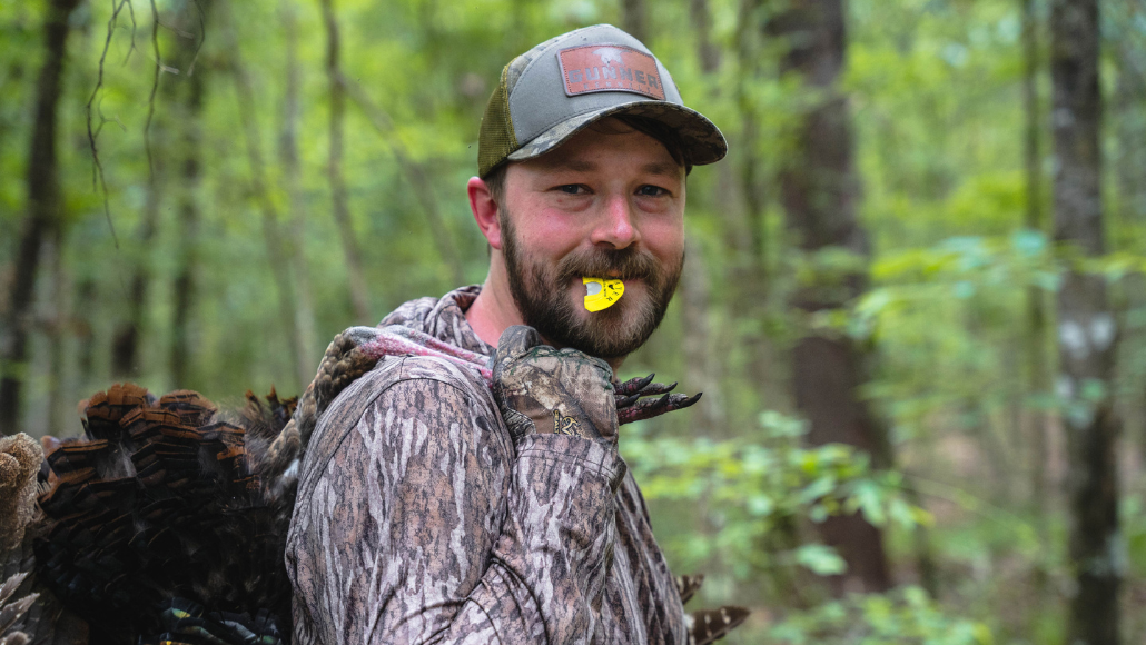 Turkey hunter with Slayer's Black Batwing in his mouth carrying harvested wild turkey