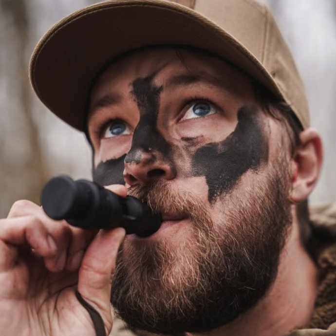 Duck hunter with camo face paint using a black Slayer duck whistle — designed to mimic pintail, teal, wigeon, and drake mallard sounds for versatile calling in the field.