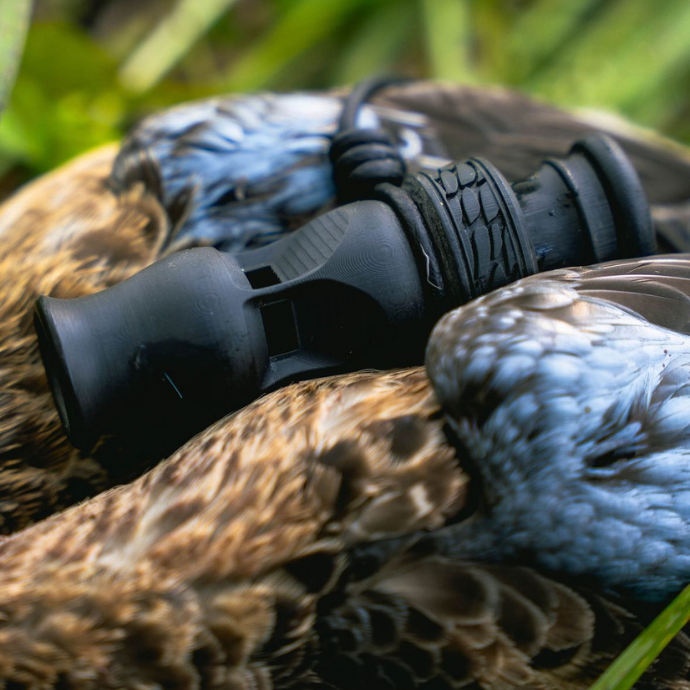 Slayer duck whistle in matte black, designed with dual side ports to produce realistic drake mallard, pintail, wigeon, and teal sounds — pictured on harvested waterfowl.