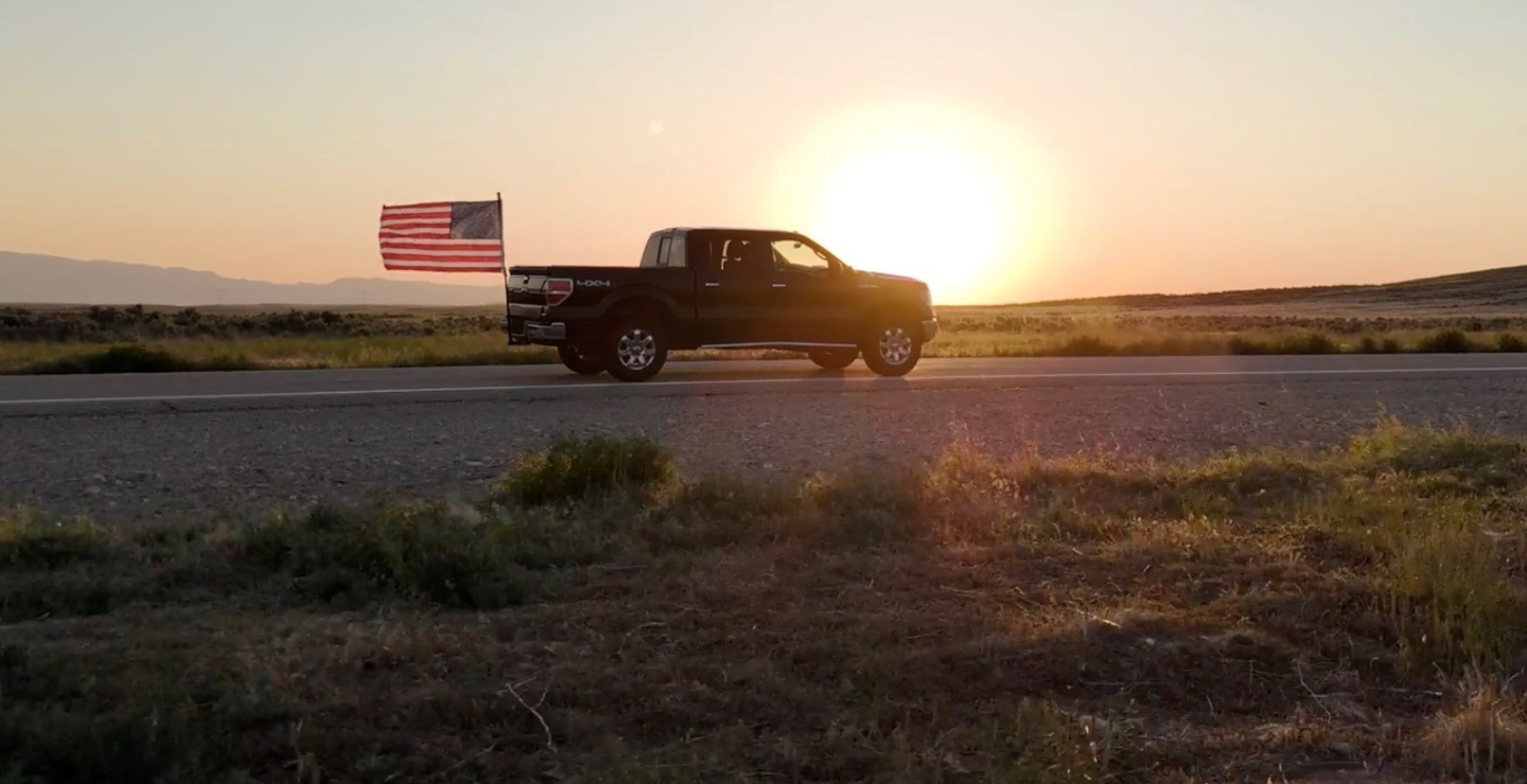 Truck on a road with an American flag at sunset