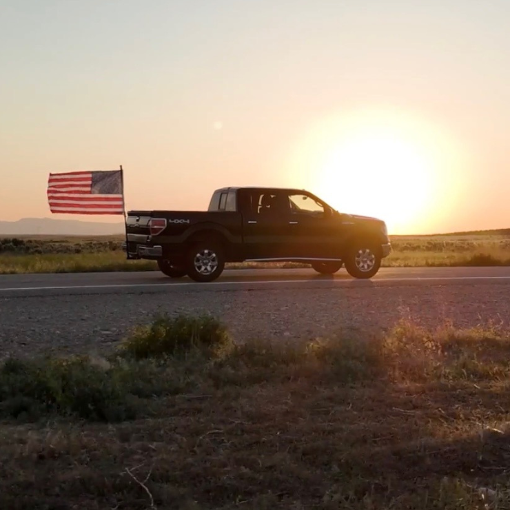 Truck on a road with an American flag in the sunset
