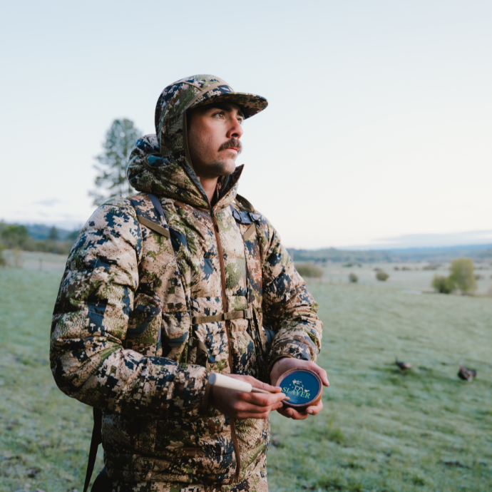 Turkey hunter in camo using Slayer's Crystal Queen pot call in a field