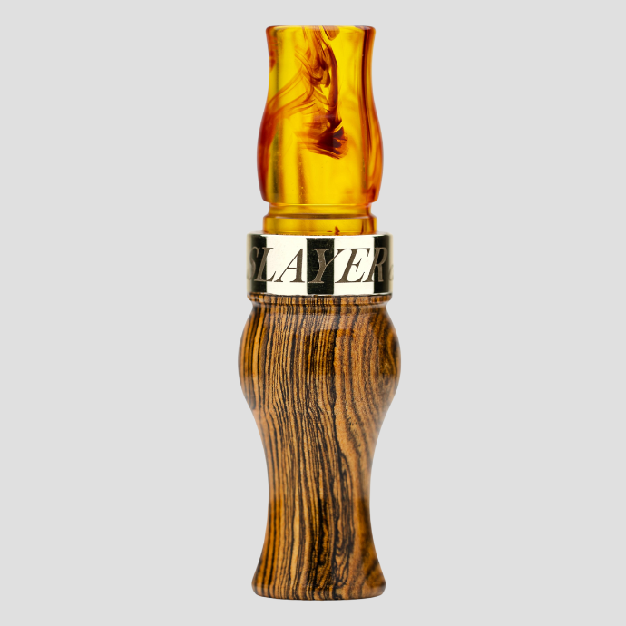 Wooden speck call with a bourbon colored acrylic insert and a brass band labeled 'SLAYER' on a gray background