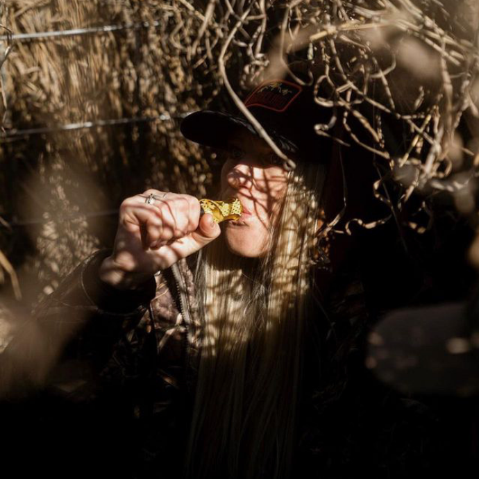 Waterfowl hunter concealed in a blind uses the Slayer DUBAR double reed duck call in Yellow Jacket Mesh, blending vibrant design with high-performance sound during a hunt.