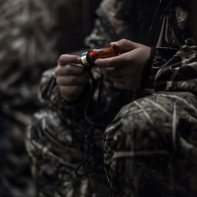 Duck hunter sitting dressed in full camo holding Slayer's Ranger duck call in citrine orange acrylic