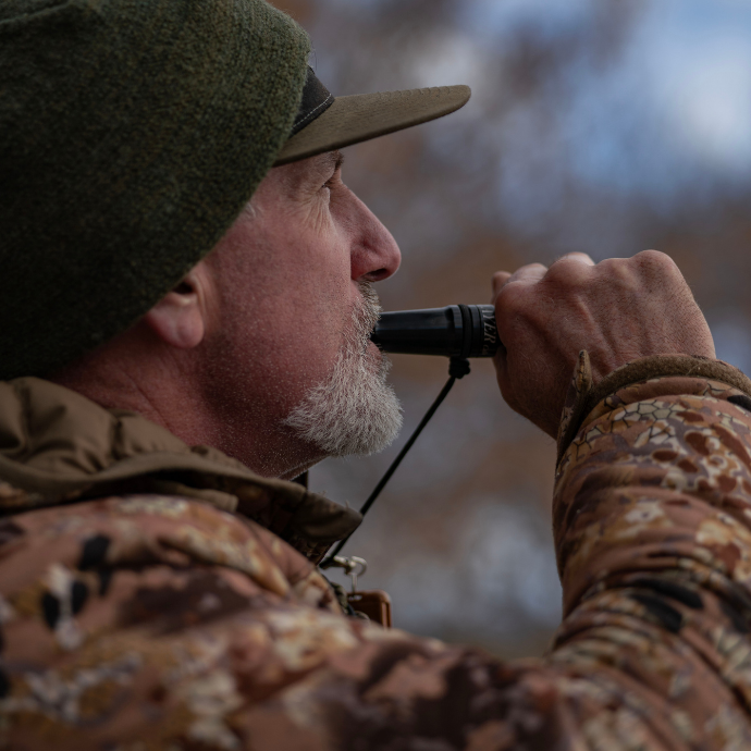Waterfowl hunter using Slayer Calls' Yolo Assassin duck call in cold-weather camo gear. The hybrid acrylic call delivers cutdown-style realism and volume, ideal for late-season duck hunts.