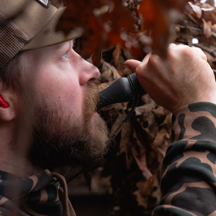 Hunter in a blind blowing Slayer’s Dagger goose call — an easy-to-use short reed call ideal for beginners mastering honks, clucks, and moans.