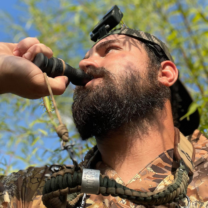 Hunter using the Slayer Calls duck whistle in the field, wearing camo and a paracord lanyard with call bands, captured during a waterfowl hunt. Part of the The Field & Stream Duck Call Collection - Slayer Duck Calls