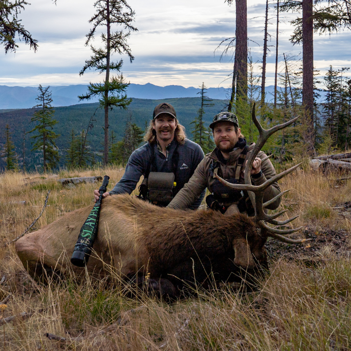 Successful elk hunt using Slayer Calls' Enchantress push button elk call and bugle combo — two elk hunters pose with mature bull elk in Montana mountains.