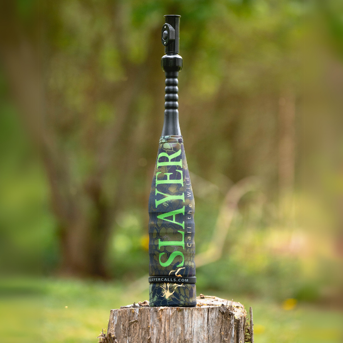The Enchantress elk call combo with Kryptek camo sleeve resting on a rustic stump in a natural field setting.