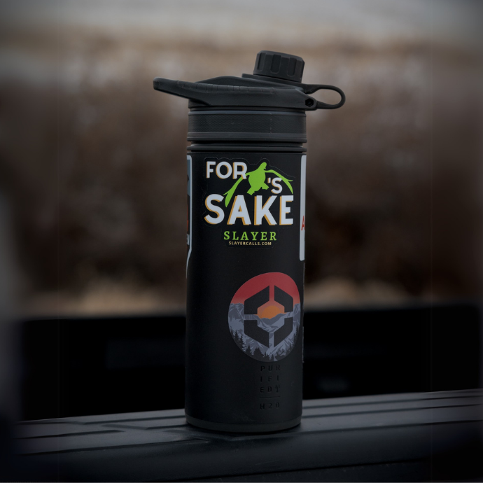 Black water bottle with custom hunting-themed stickers, including “For Duck’s Sake” and Slayer Calls branding, sitting on a truck bed with an outdoor backdrop.