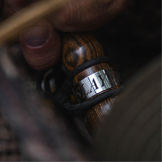 Close-up of a hunter gripping the wood-finished Slayer goose call named the Axe Slayer, secured with a paracord lanyard — precision-crafted for lifelike honker sounds in the field.
