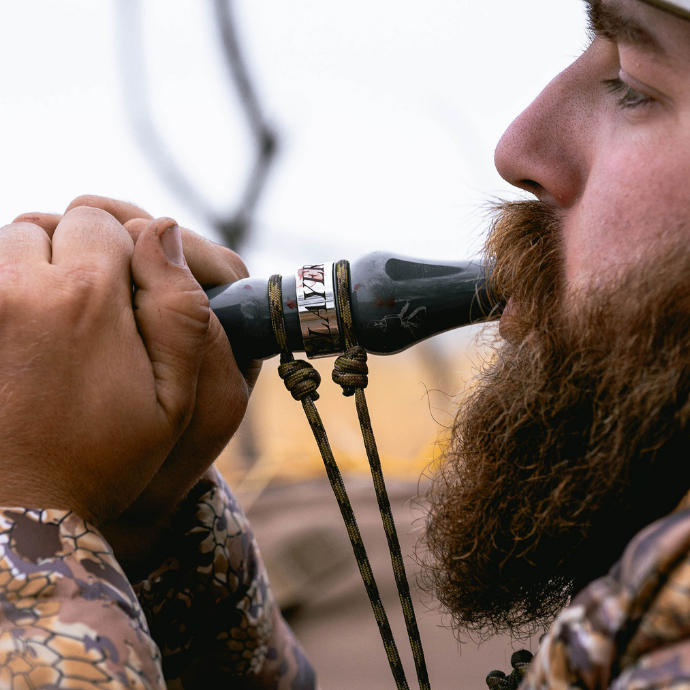Hunter using the Slayer Calls Leg Iron goose call, shown in close-up with paracord lanyard and camo jacket — built for realistic Canada goose sounds in the field.