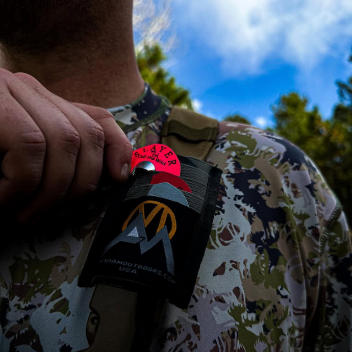 Close up shot of an elk hunter sliding Slayer's hot pink Isabella Creek elk reed into a reed carrier on his pack.