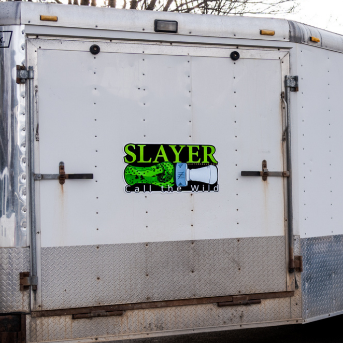 Illustrated Slayer Calls trailer decal featuring a green duck call with tally marks and bold horizontal “SLAYER” text, alongside the brand’s slogan “Call the Wild.” Pictured on the backside of a trailer.
