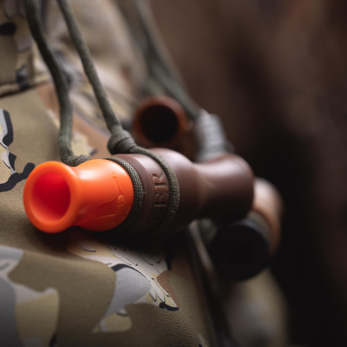 Close-up of a rice wrecker speck call with orange insert on camouflage fabric.