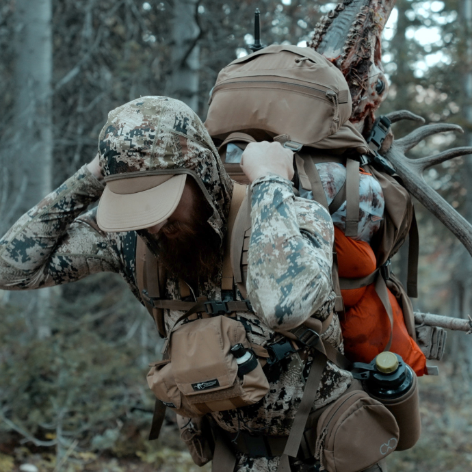 Elk hunter packing out harvested bull elk after using Slayer Calls’ ArchAngel bugle tube and Clearwater Series Elk reeds. Backdrop is a rugged mountain terrain in the Idaho wilderness.