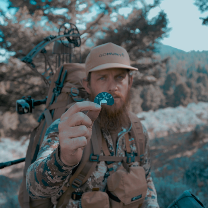 Close-up of elk hunter in camo using Slayer’s blue Locsha elk reed, included in the River Series. The Archangel bugle tube visible in his pack.