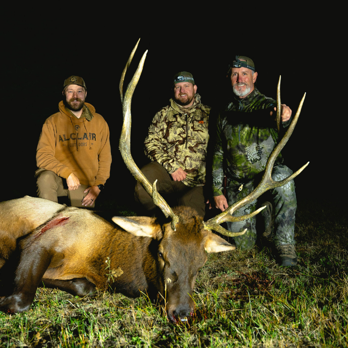 Trio of elk hunters, including Slayer CEO, Bill Ayer kneeling behind a mature bull elk after a successful elk hunt using Slayer's Clearwater Series Elk reeds and ArchAngel bugle tube