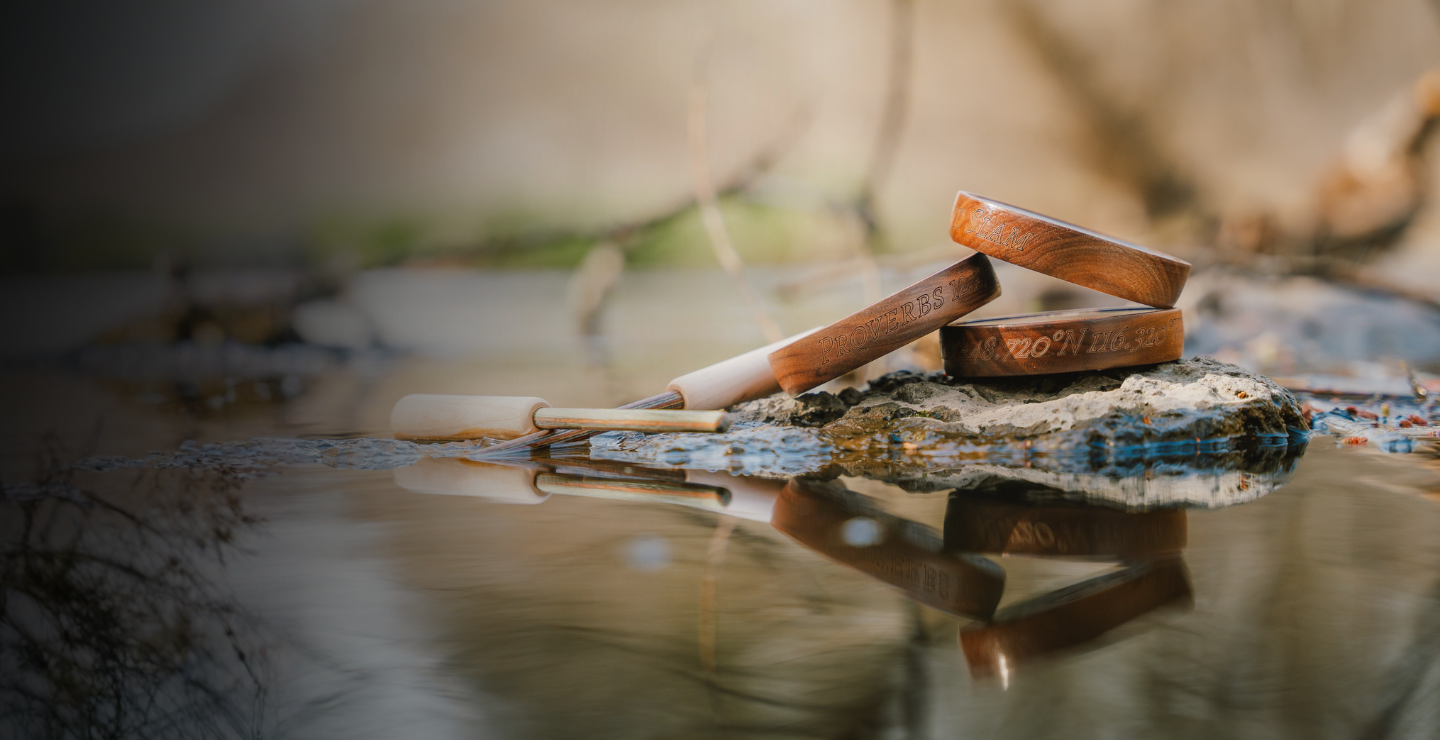 Custom pot calls with engraved wooden rims and striker set resting on a rock by water, showcasing personalized turkey hunting calls designed for performance and meaningful customization.
