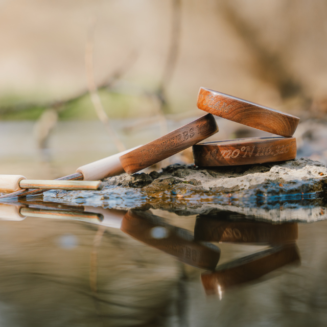 Custom pot calls with engraved wooden rims and striker set resting on a rock by water, showcasing personalized turkey hunting calls designed for performance and meaningful customization.