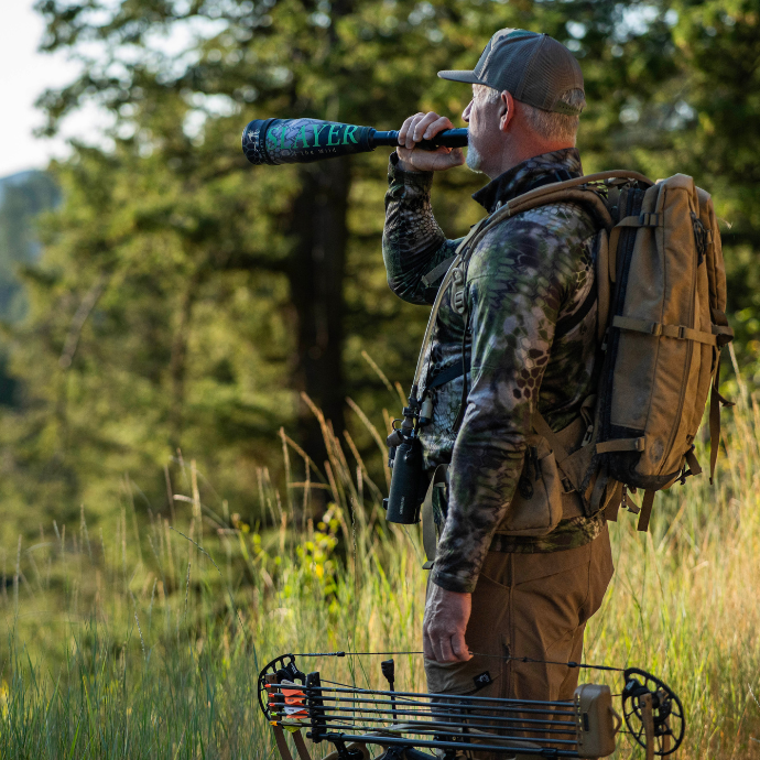 Hunter in camouflage gear with a bow, blowing Slayer's Enchanted Lil' Warrior in a forest setting