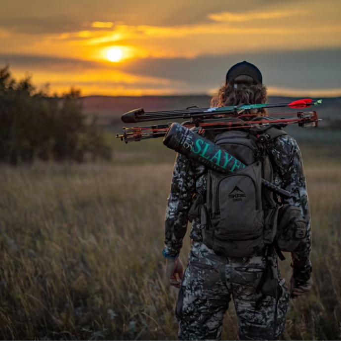 Backcountry elk hunter at sunset carrying a compound bow and Slayer bugle tube, ready for archery season in open terrain.