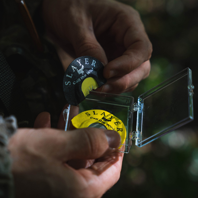 Hunter holding Slayer’s Snake Bite and Black Batwing diaphragm turkey calls, shown stored in a protective clear case during a hunt. These turkey calls are part of The Slayer Sweet Talk’r Kit - Slayer Calls
