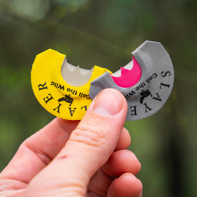 Hunter holding Slayer’s Black Batwing (yellow) and Grey Batwing (grey) turkey diaphragm calls — precision-cut latex for realistic hen vocalizations.