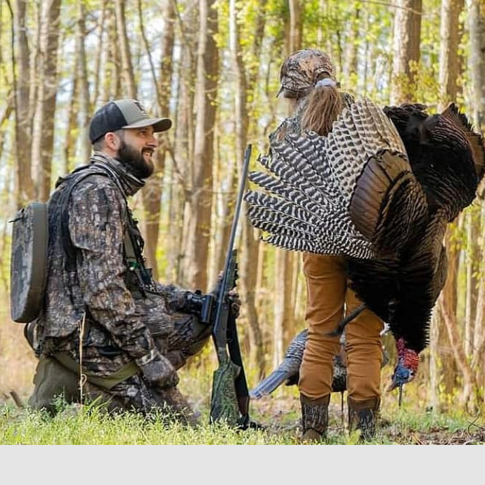 Father and daughter turkey hunting with daughter holding harvested turkey over her shoulder