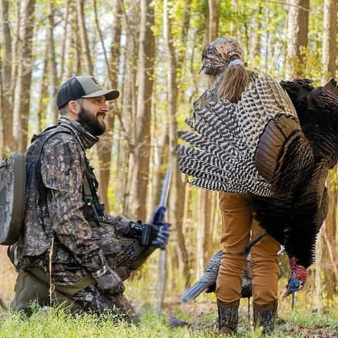 Father and daughter turkey hunting with daughter holding harvested turkey over her shoulder