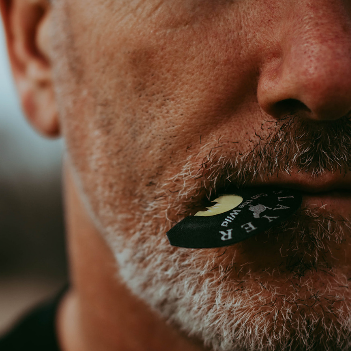Close-up of a hunter with gray stubble using the Slayer Snake Bite diaphragm turkey call, gripped between his lips in preparation for calling.