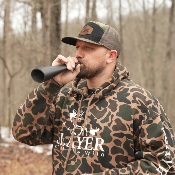 Hunter in camo hoodie using the Gobbler Slayer turkey call in the woods during spring turkey season.