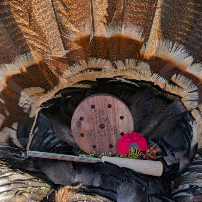 Slayer Calls’ Crystal Queen turkey pot call and Quad Hen mouth call displayed on turkey fan with striker and feathers.