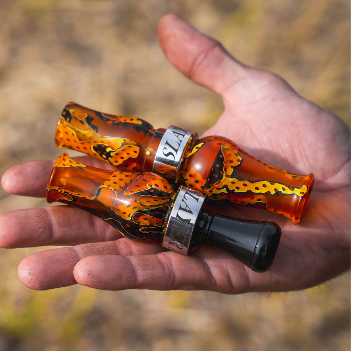 Slayer’s Honker Slayer goose call and Ranger duck call in vibrant Orange Mesh acrylic finish with polished Slayer bands, displayed in a hunter’s hand.