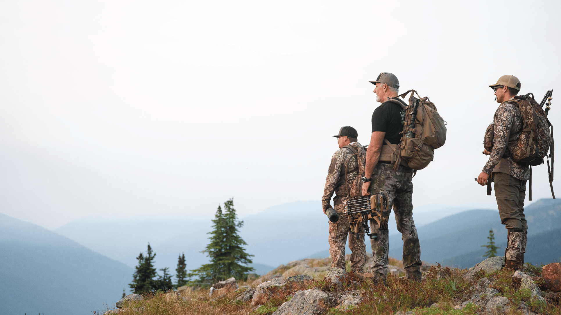 Three archery elk hunters standing on bluff overlooking the mountains of British Columbia, Canada.