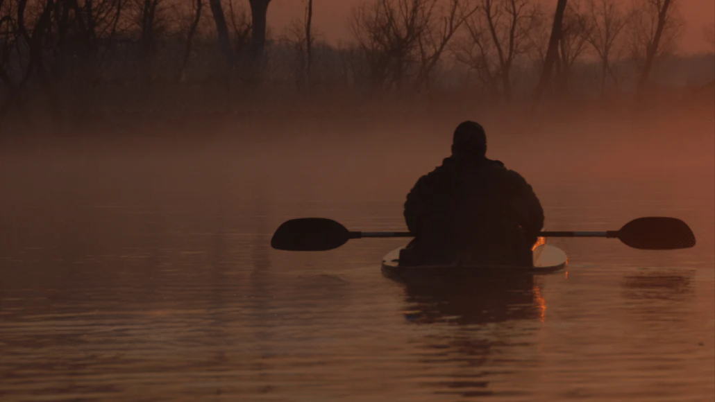a person in a kayak paddling through the water at sunset