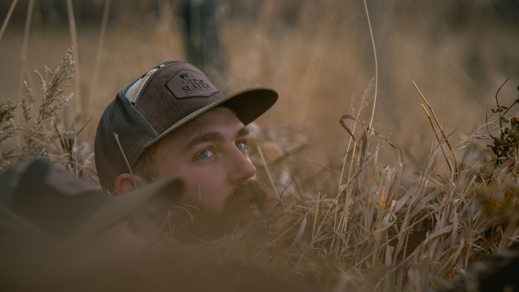 Waterfowl hunter wearing Slayer camo hat in a layout blind