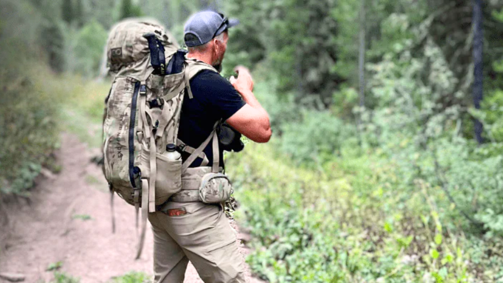 An elk hunter with a backpack scouting during on a trail.