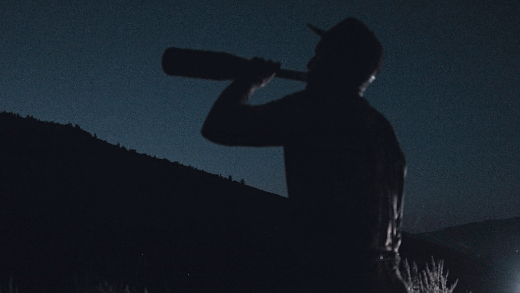 a silhouette of an elk hunter blowing a bugle tube in the dark