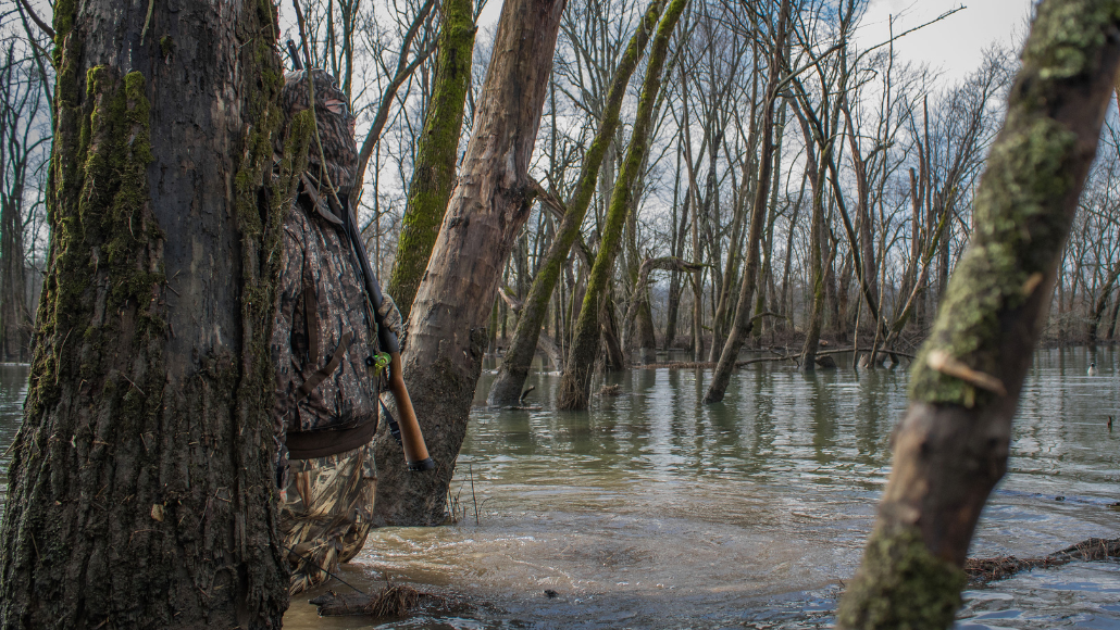 Duck hunter concealed in full camo next to tree in the water
