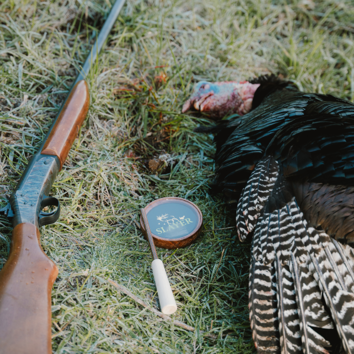 Slayer's Crystal Queen turkey pot call with green and gold logo next to a freshly harvest tom. 