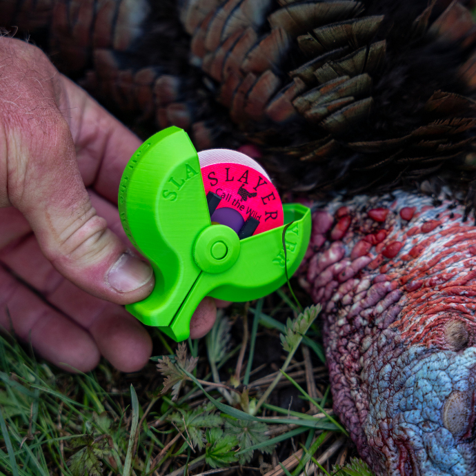 Turkey hunter holding the Slayer green reed holder with a hot pink turkey mouth reed adjacent to a freshly harvested turkey.