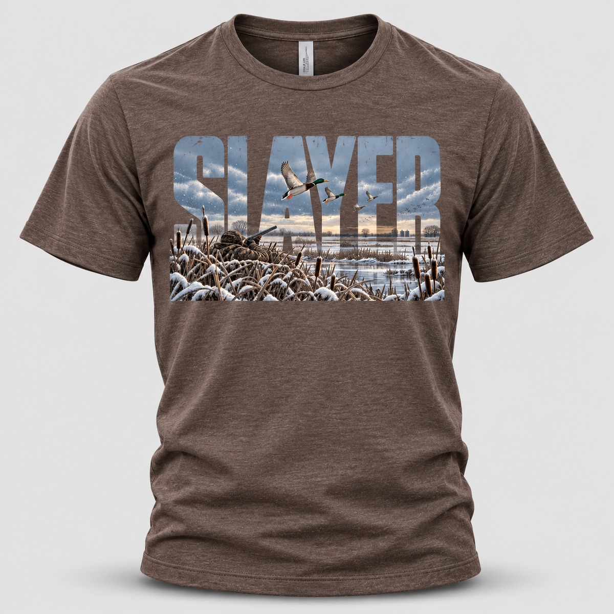 Front view of a heather brown Slayer Calls T-shirt featuring bold SLAYER lettering with a snowy duck hunting scene, flying mallards, a camouflaged hunter, and frost-covered marsh grasses.