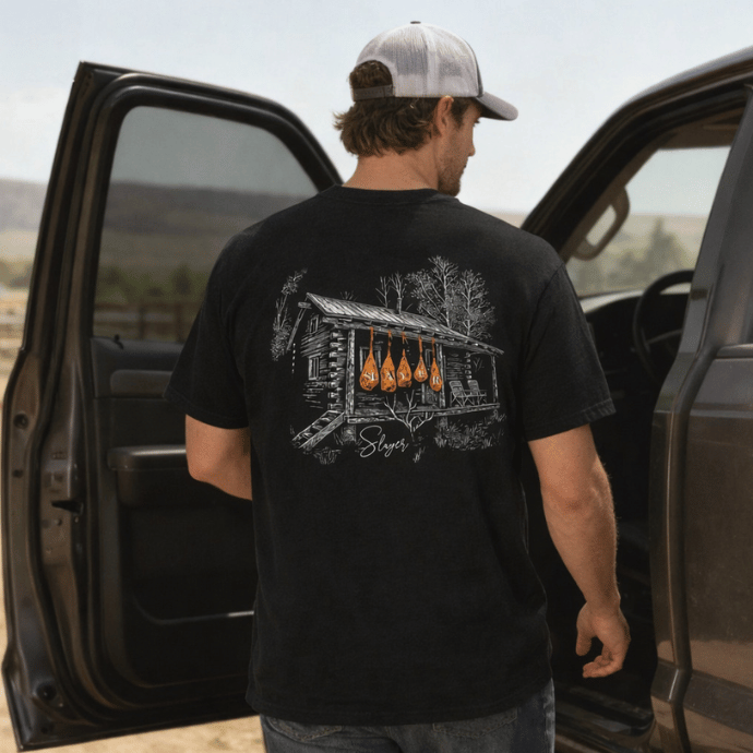 Man getting into a truck with a black t-shirt with a cabin sketch and orange SLAYER game bags hanging on the porch.