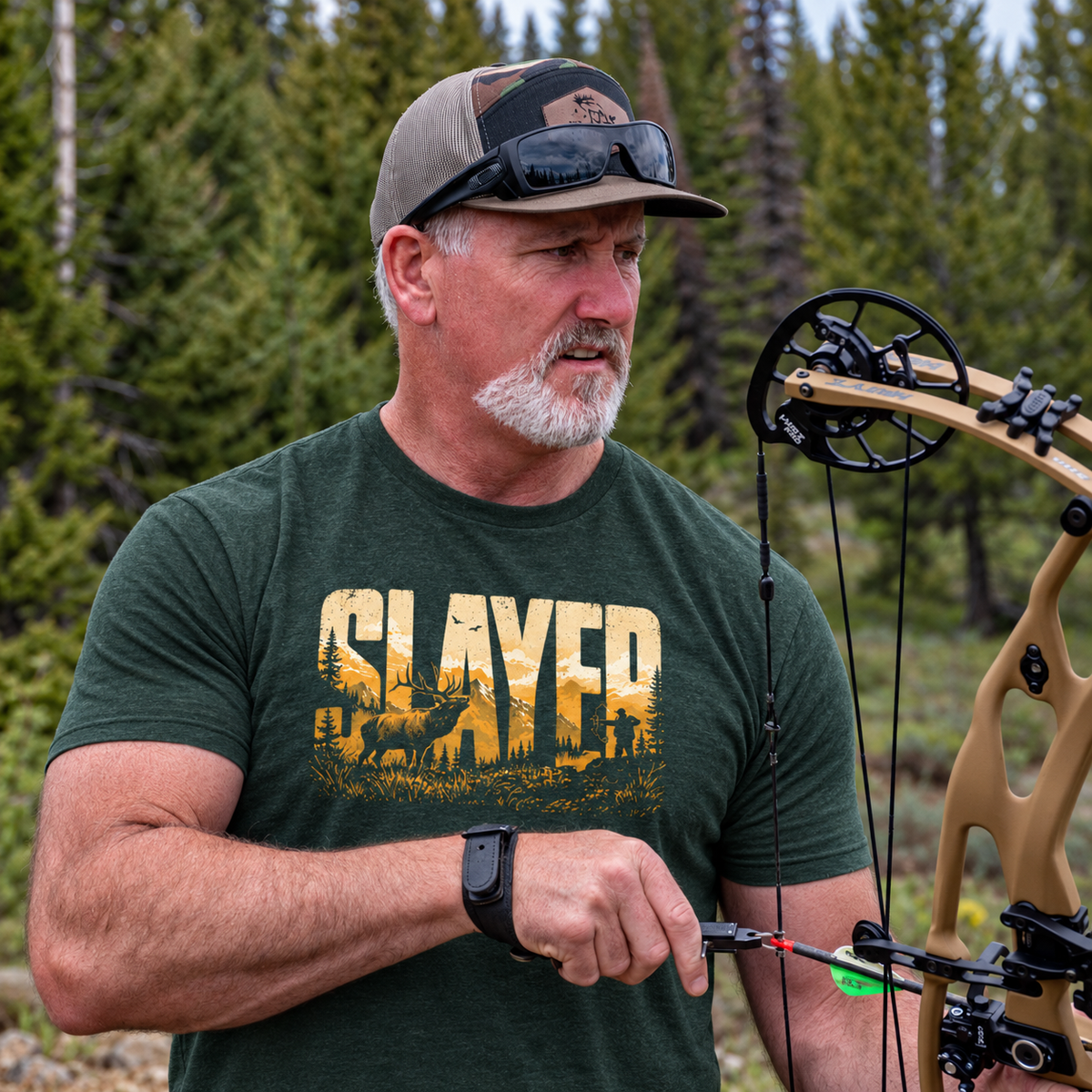 Bill Ayer wearing a forest green Slayer Ridgeline T-shirt and holding a compound bow in an evergreen forest.