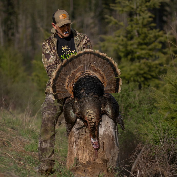 Slayer team member Joe McCarthy in camouflage holding a large turkey in a forest setting