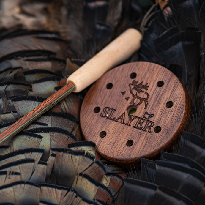 Wooden pot call with 'SLAYER' branding placed on the fanned tail feathers of a freshly harvested spring turkey. 