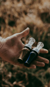 Hunter's hand with two duck calls: the Suzie Slayer Duck Call and the Drake Slayer Duck call