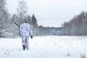 hunter with shotgun walking in the snowy winter field